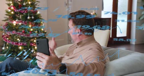 Man holding smartphone on sofa gesturing with christmas tree and financial data overlays