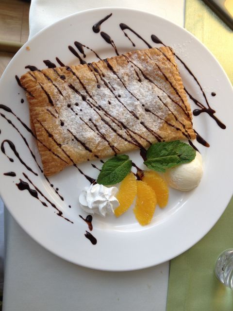 Gourmet pastry topped with powdered sugar and chocolate drizzle, accompanied by fresh orange slices, whipped cream, vanilla ice cream scoop, and mint leaves. Perfect for food blogs, restaurant menus, social media promotions, and culinary magazines showcasing elegant desserts.