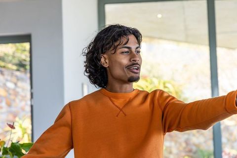 Indian man pointing toward glass doors in modern home wearing orange sweatshirt