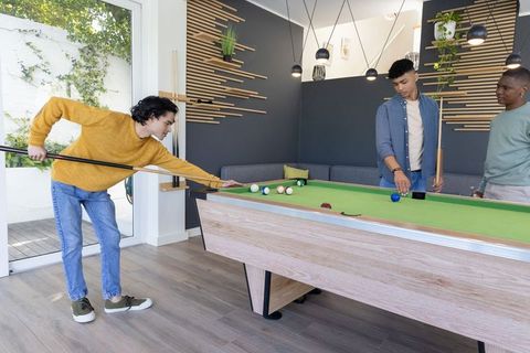 Three friends playing pool in contemporary home game room with green felt table