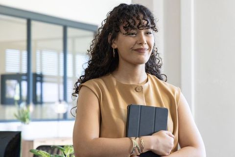 Confident young professional holding tablet in modern glass-partition office, smiling