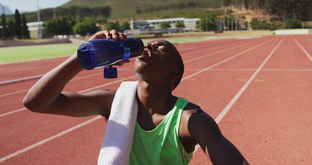 African american male athlete sitting and drinking water at empty stadium - Download Free Stock Photos Pikwizard.com