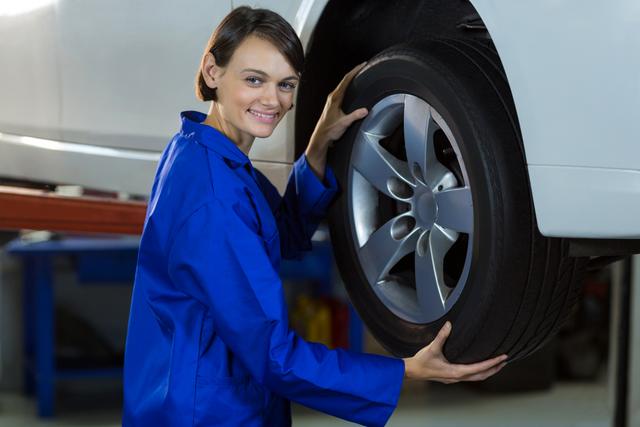 Portrait of female mechanic fixing a car wheel in repair garage