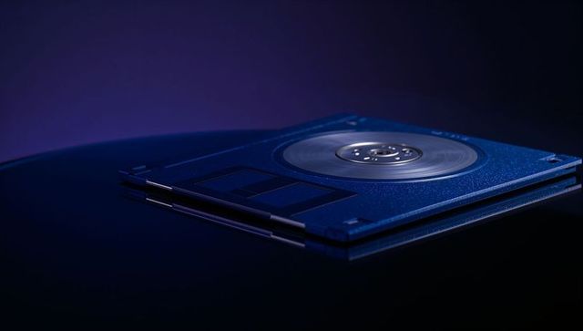 Displaying 3.5-inch floppy disk with translucent shell and metallic hub on glossy surface