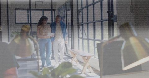 Coworkers walking and reviewing documents in sunlit modern office with grid windows