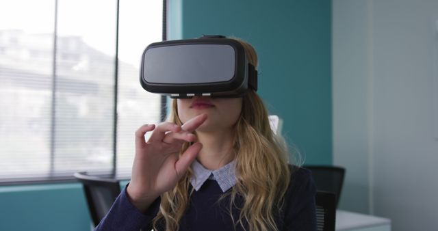 Young woman exploring virtual reality with a VR headset in a modern office. Suitable for illustrating themes related to technology, future of work, tech trends, innovation, and digital experiences. Can be used in advertising campaigns, blog posts, tech articles, or business presentations.