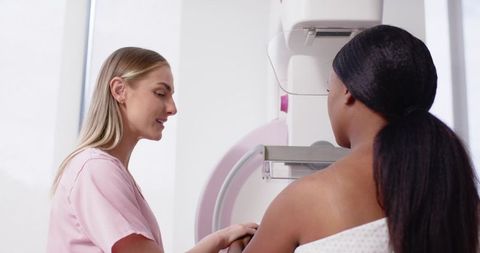 Technician positioning patient for mammography breast screening in bright radiology clinic