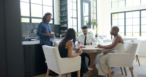 African american friends chatting and sharing drinks around table in sunlit modern kitchen