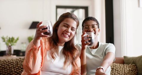 Cozy coffee toast: friends laughing on sofa, casual duo sharing warm home moment