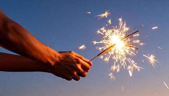 Hands holding sparkler at twilight, glowing golden sparks creating warm evening mood