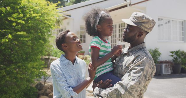 Happy african american male soldier and his family embracing and smiling outside the house. Military, patriotism, family, and togetherness.