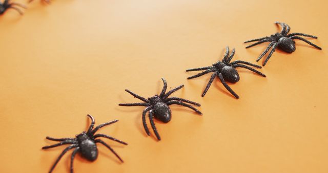 Plastic spiders aligned on an orange background. Ideal for Halloween decorations, spooky arts and crafts, and themed social media posts. Useful for creating festive holiday invitations, blog visuals, or promotional materials for Halloween-related events.