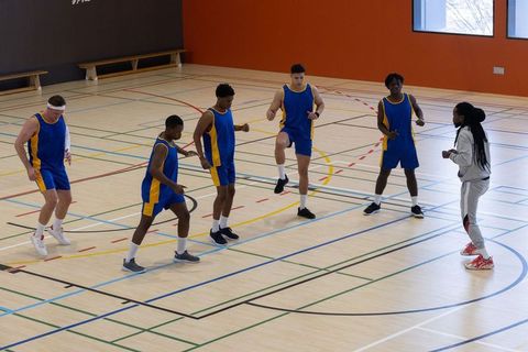 Basketball team warming up on indoor court with coach