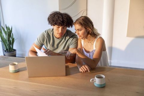 Young Couple Reviewing Bills and Working Together on Laptop in Bright Minimalist Home