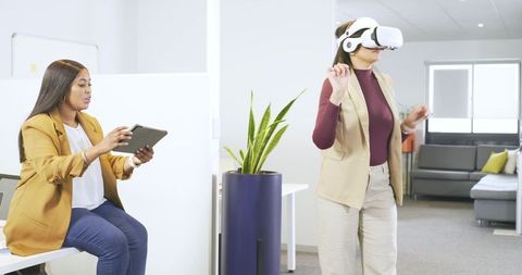 Coworkers testing virtual reality headset while colleague controlling tablet in office