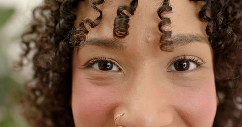 Closeup smiling woman with curly hair wearing gold nose hoop and natural rosy makeup
