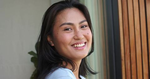 Young asian woman turning head smiling by window natural light closeup portrait with ear studs