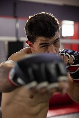 Mid-30s mma fighter throwing straight punch in cage gym showing intense focus and power