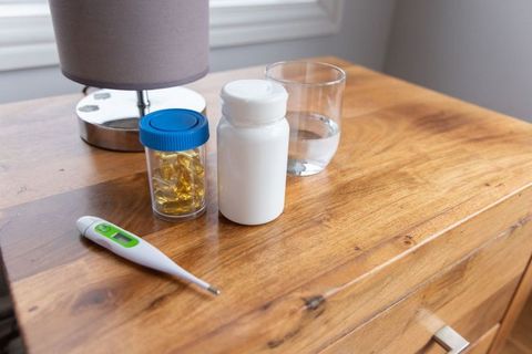 Nightstand medication with white pill bottle, softgels, water glass and thermometer