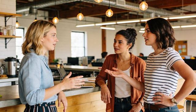 Three women collaborating and brainstorming at modern open-plan office counter with laptop