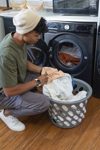 African american man loading front-load washer in modern laundry nook, sorting clothes
