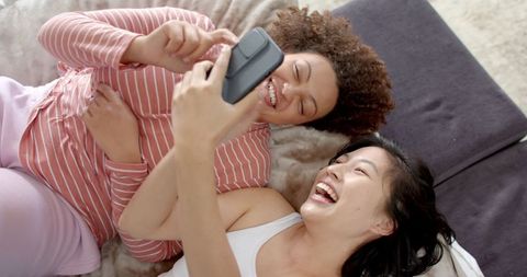 Diverse Friends Laughing on Cozy Sofa with Smartphone