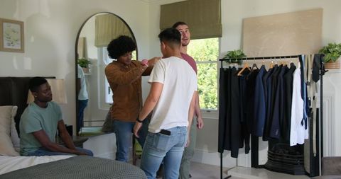 Friends helping groom choose wedding suit at home