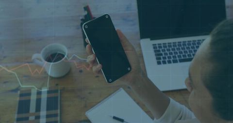 Woman focusing on smartphone at work desk with coffee