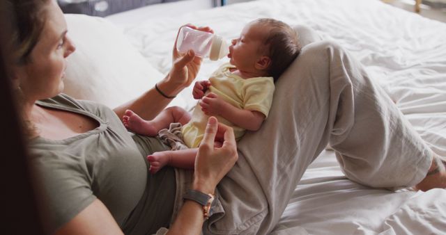 Image of happy caucasian mother feeding newborn baby with bottle on bed. motherhood, parental love and taking care of newborn baby concept digitally generated image.