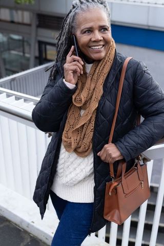 Senior african american woman smiling and talking on phone in urban walkway wearing quilted coat