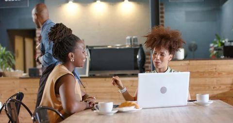 Women collaborating over laptop and coffee in modern cafe coworking space during casual meeting