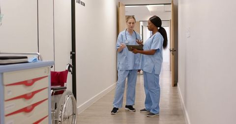 Nurses consulting with tablet in clinic corridor reviewing patient records and care plan