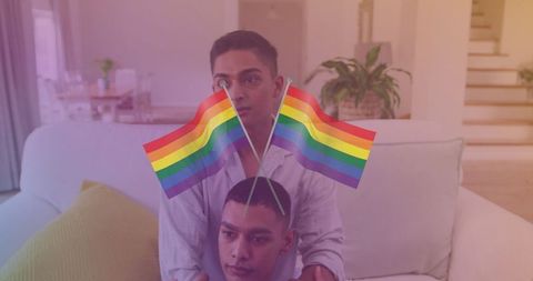 Happy biracial gay couple with rainbow flags at home