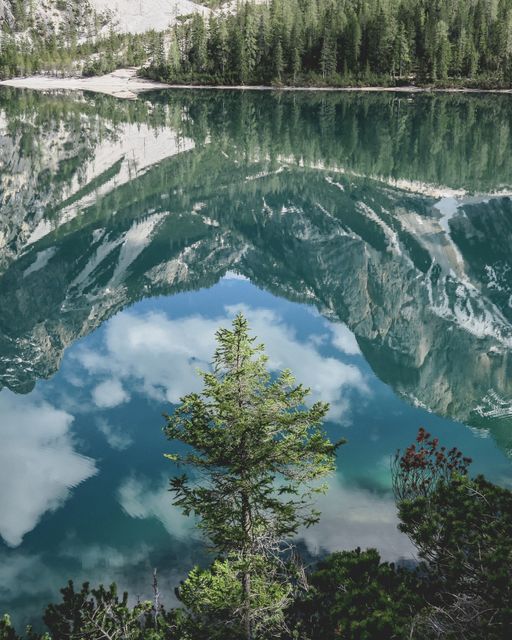 Scenic view of a serene mountain lake perfectly reflecting the surrounding forest and peaks. Ideal for use in travel, nature, and outdoor adventure magazines or blogs. Can also be useful for promoting eco-tourism or as inspiration for landscape photography.