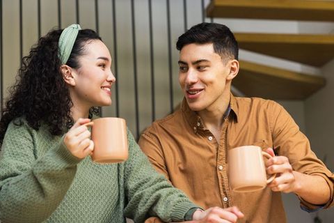 Young couple sharing coffee and conversation in cozy living room with staircase