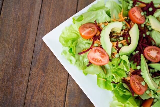 Fresh vegetable salad featuring avocado slices, cherry tomatoes, and mixed greens on a white plate. Ideal for use in health and wellness blogs, nutrition articles, vegan and vegetarian recipe websites, and food-related marketing materials.