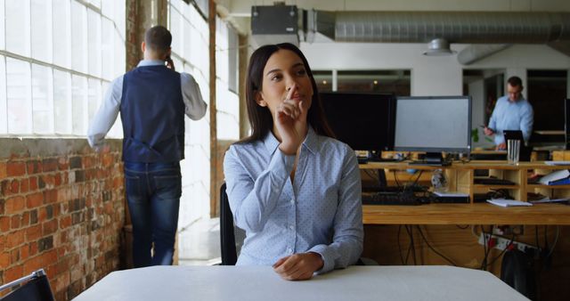 Young woman in modern office thinking with colleagues in background - Download Free Stock Images Pikwizard.com