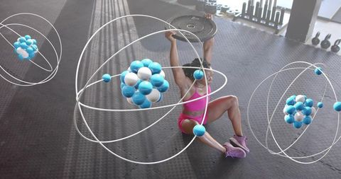 Woman pressing weight plate overhead while sitting on gym floor with orbit atom graphics