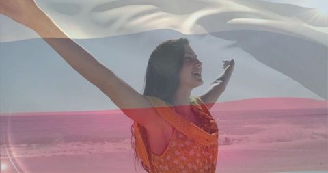 Woman embracing ocean breeze with translucent flag overlay, smiling toward sunlit shore