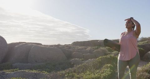 Woman Holding Yoga Mat on Rocky Shore Gazing Into Horizon