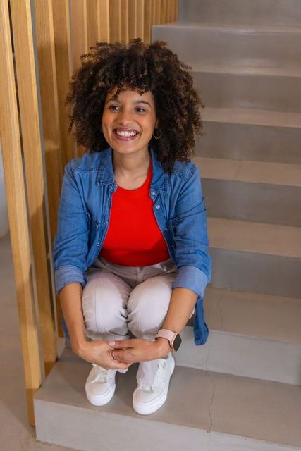 Happy african american woman sitting on stairs smiling wearing denim and smartwatch casual