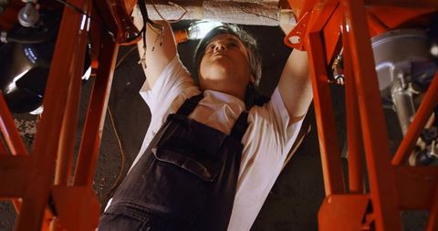 Mechanic inspecting undercarriage under red lift with headlamp for auto repair