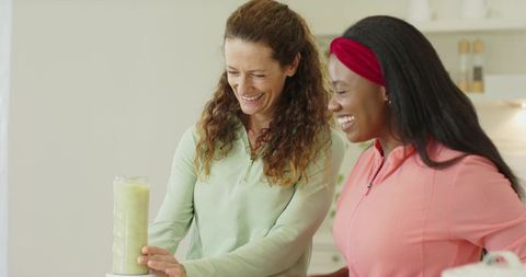 Diverse women blending smoothie in kitchen with joyful expressions