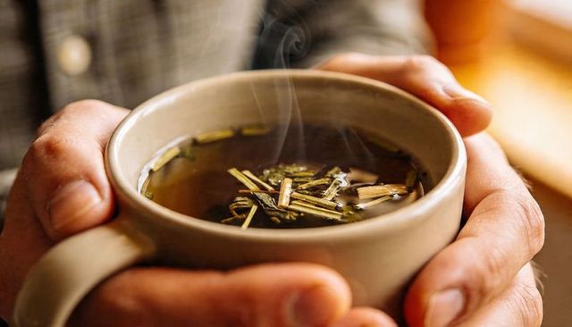 Hands cradling steaming lemongrass tea in ceramic mug near window for cozy moments