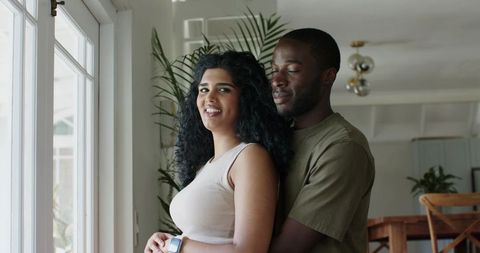 Young couple embracing by sunlit window in cozy plant-filled living space