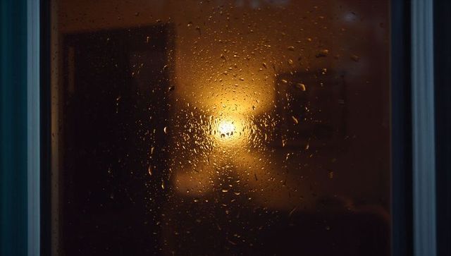 Glistening Rain-Dappled Window Revealing Warm Lamp Glow Through Condensed Night Pane