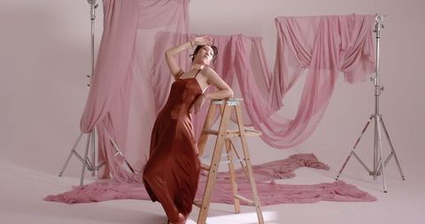Asian female model elegantly posing amid draped pink curtains in fashion studio