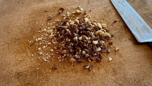 Chopping peanuts and raisins on rustic wooden cutting board with chef knife