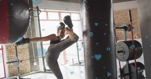 Athletic woman delivering high roundhouse kick to heavy bag during dynamic gym training