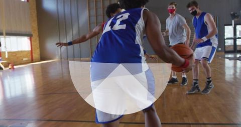 Basketball player dribbling in gym with masked opponents